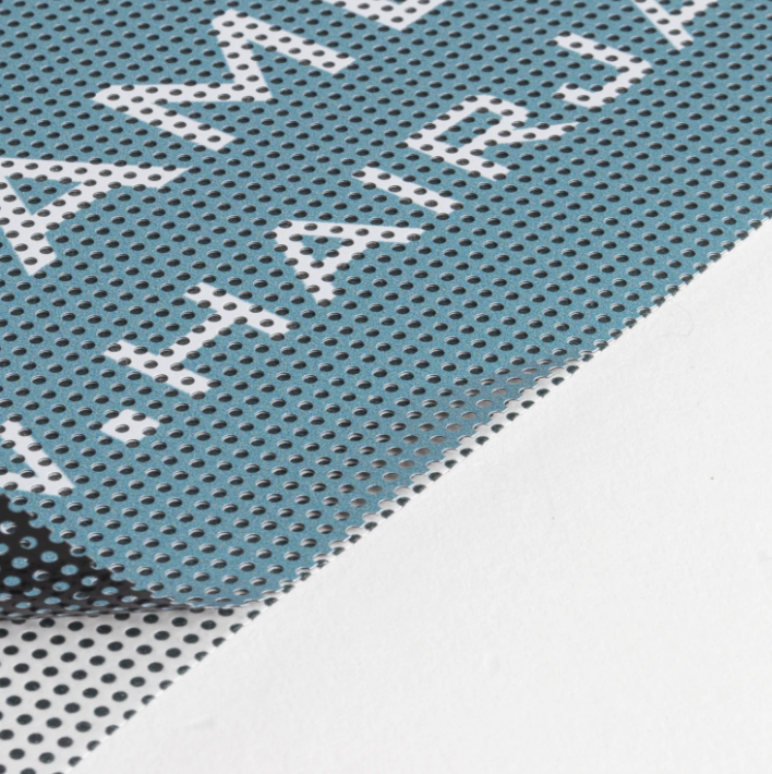 A close-up of a light blue perforated mesh sheet with white text reading 'HAIR JAM' and a black mesh layer partially visible underneath on a white surface.
