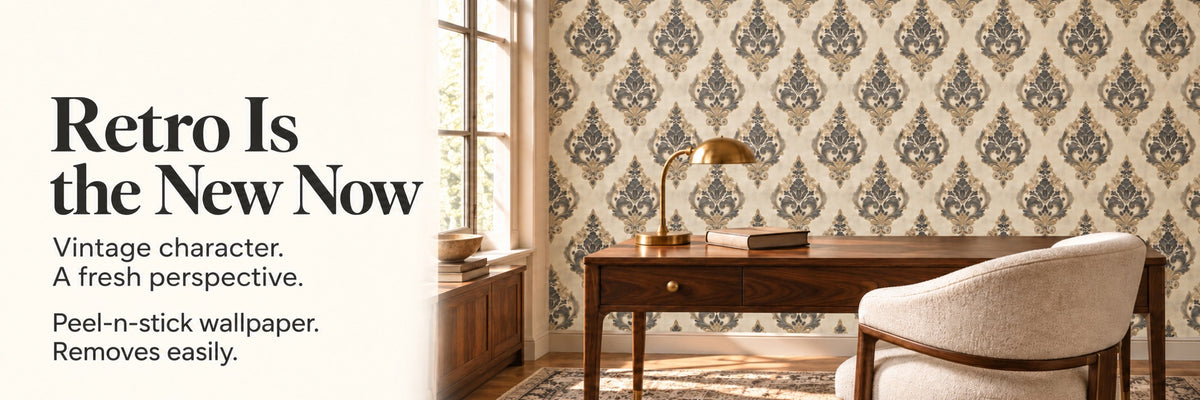 Vintage damask peel-and-stick wallpaper behind a wooden desk with a brass lamp and armchair
